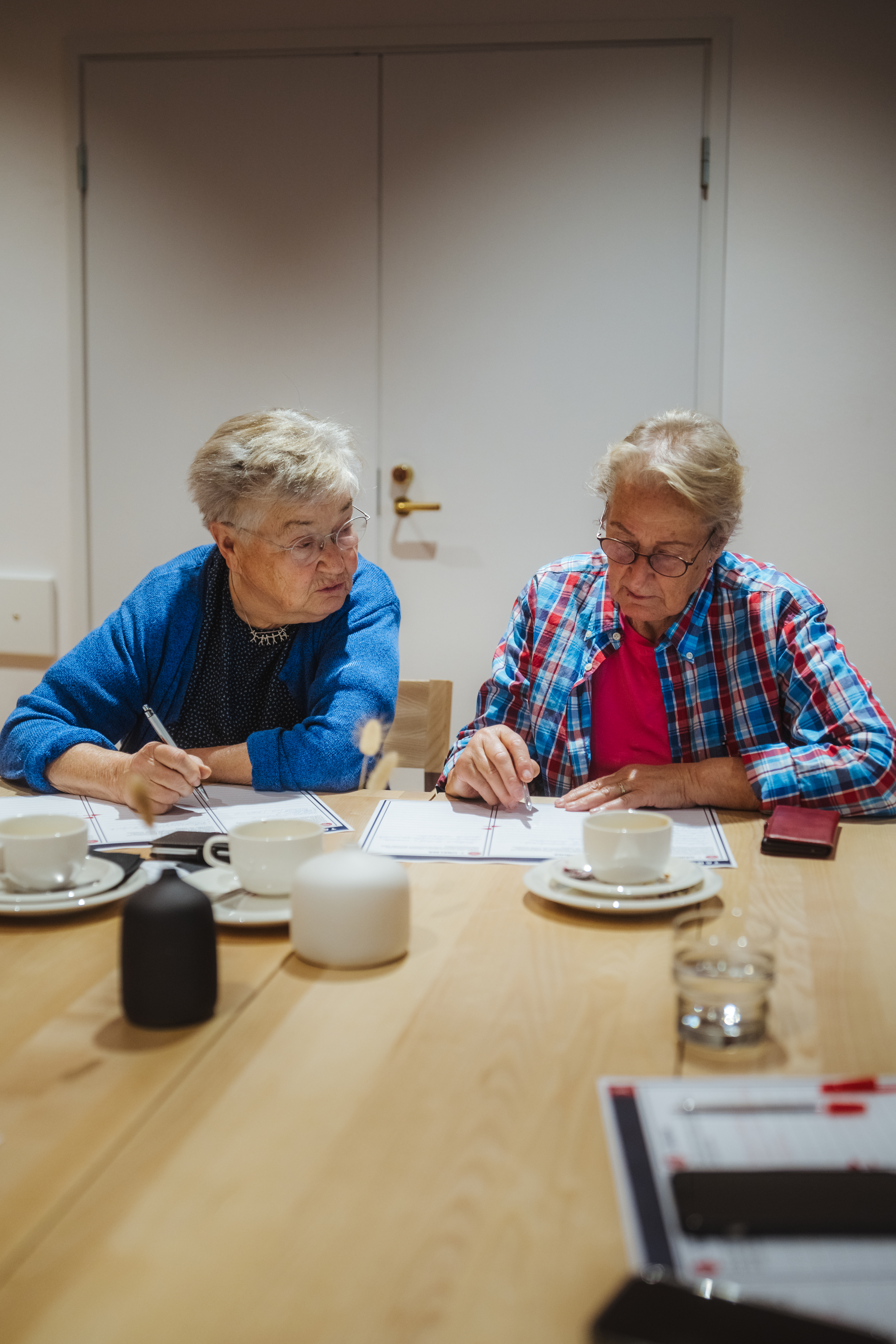Kaksi mummoa pohtii kysymyksiin vastauksia pöydän ääressä.