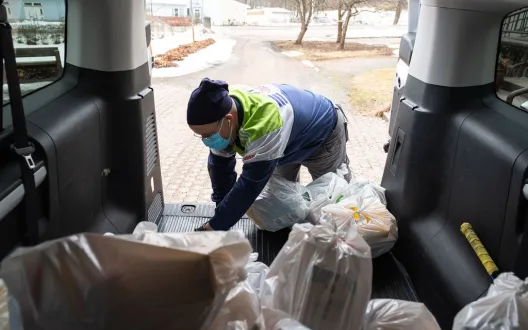 Henkilö tyhjentää elintarvikekasseja auton tavaratilasta.