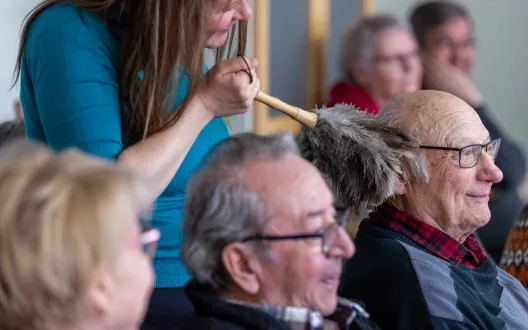 Kuvassa nainen kutittelee seniorin hiuksia huiskulla. 