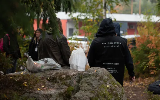 Kaksi etsivän työn ohjaajaa seisoo metsässä, keskellä on valkoinen muovikassi