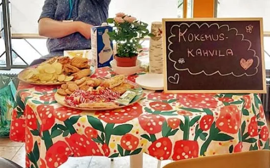 Kuvassa on pöytä, jossa kahvila tarjoiluja. Pöydän takana on lippispäinen mies.