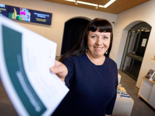 Hymyilevä tummahiuksinen nainen ojentaa kulttuurireseptiä. Taustalla taidemuseon museokauppa.