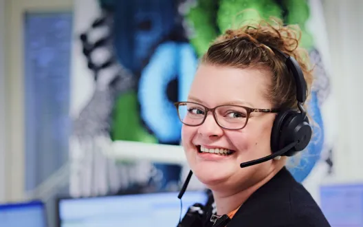 Kuvassa hymyilevä  henkilö, jolla kuulokemikrofoni.  