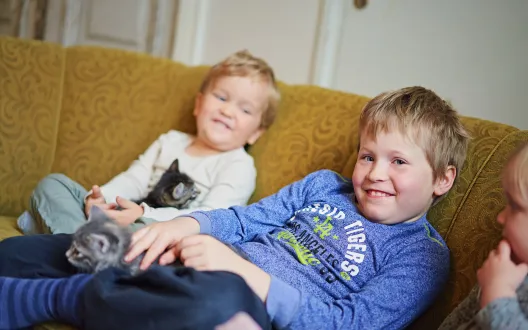 kuvassa kaksi hymyilevää lasta istuu sohvalla.