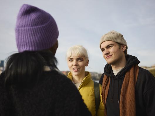 Yksi henkilö selin ja kaksi henkilöä kasvot näkyvissä.