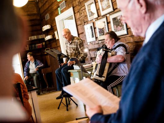 Singsongs in the Lähteentien Pirtti, old building. Old male singing, old male playing accordion.