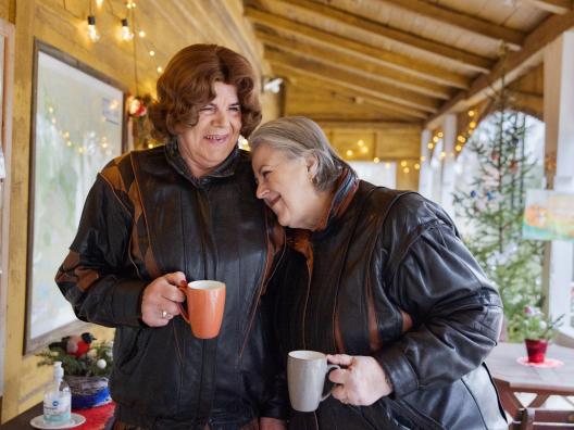 Kaksi naisoletettua henkilö ovat samanlaiset nahkatakit päällä katoksen alla, jossa on kausivalot kahvikupit kädessään