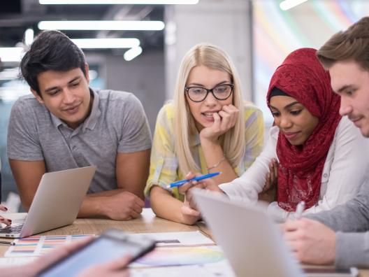 Kehittäjät seisovat pöydän ääressä keskustellen ja pohtien. Pöydällä on papereita ja tietokone.