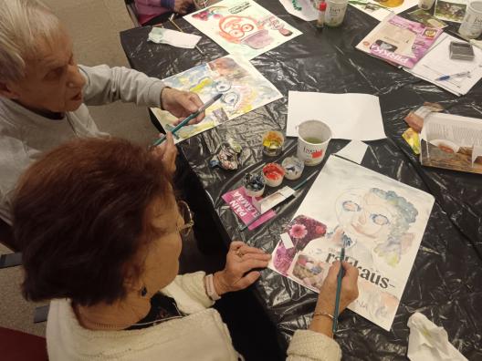 Kuvassa ikääntynyt pariskunta tekee kollaasityötä mm. akvarelleilla, lehtileikkeillä.