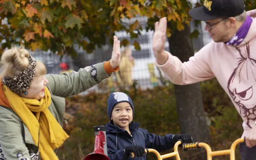 Kuvassa mies ja nainen lyövät ylävitoset samalla kun kouluikäinen poika katselee ja hymyilee taustalla heidän välissään.