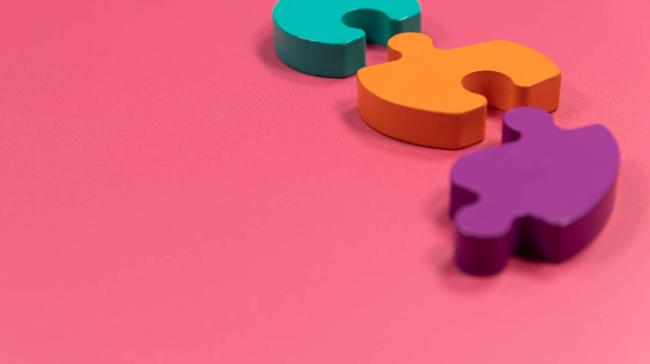 Pinkillä pohjalla kolme eri väristä palapelin palaa.