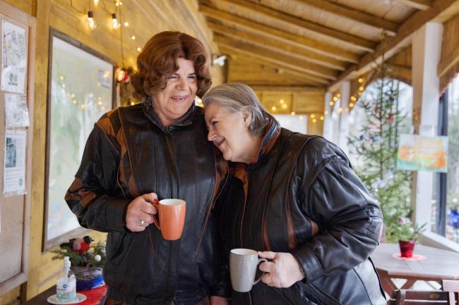 Kaksi naisoletettua henkilö ovat samanlaiset nahkatakit päällä katoksen alla, jossa on kausivalot kahvikupit kädessään